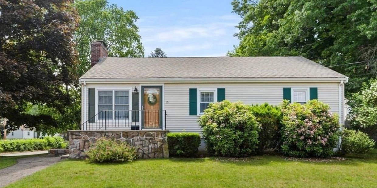 Small white house with green shutters and front bushes.