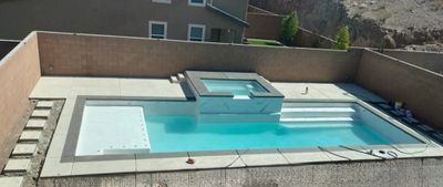 A modern rectangular swimming pool with an attached hot tub in a backyard.