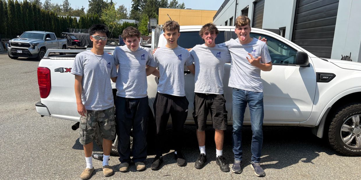 Five young men in matching gray shirts posing in front of a white pickup truck.