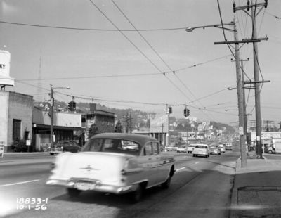 Black and white image of a 1950s street with vintage cars.