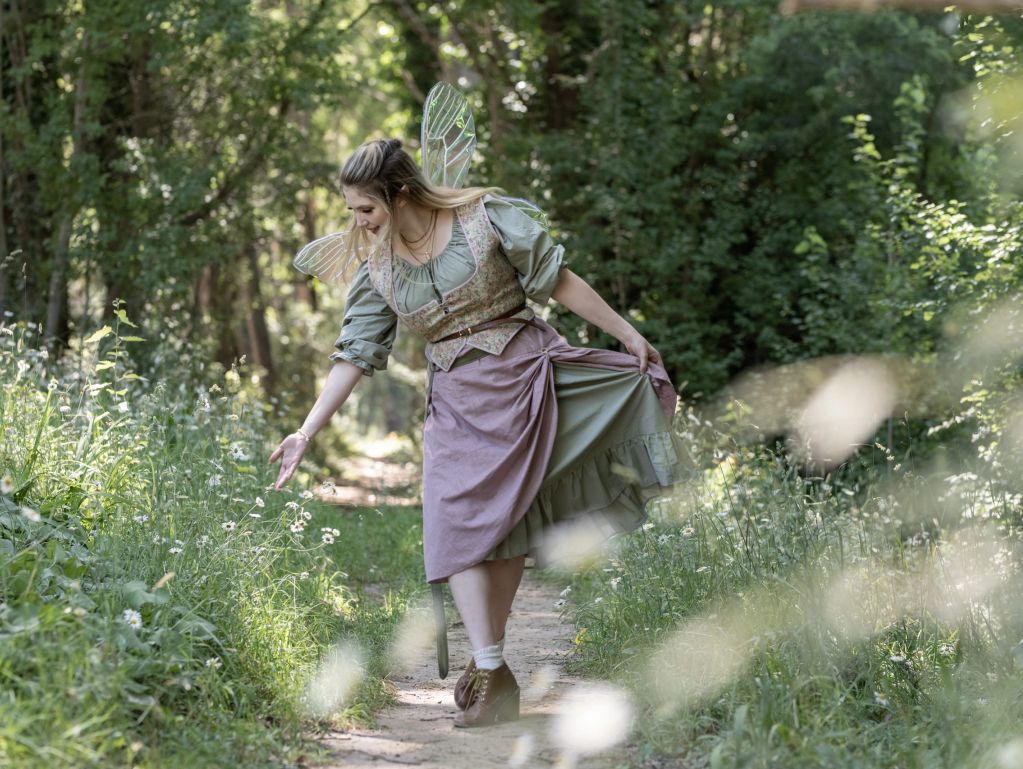 Woman in fairy-like costume walking through a forest path.