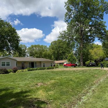 Sunny suburban yard with trees, red truck, and worker near a lawn mower.