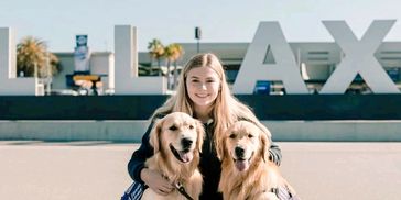 Young woman with two golden retrievers in front of LAX sign.