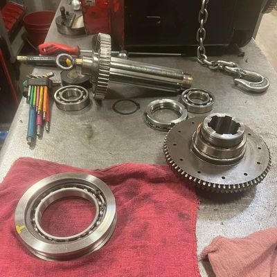 Disassembled mechanical parts and tools on a metal workbench with red cloths.