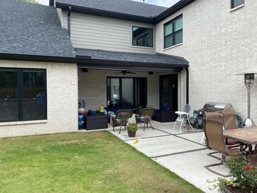 Backyard patio with seating, grill, and dining area beside a modern house.