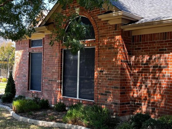 Brick house exterior with black window shutters and garden.