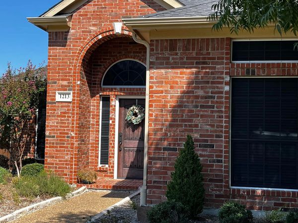 Red brick house entrance with a wooden door and decorative wreath.