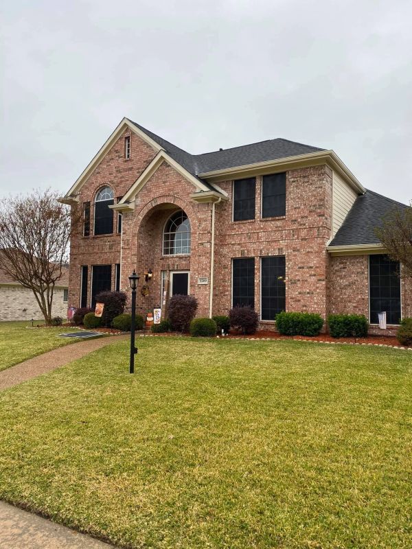 A large brick two-story house with a well-kept lawn and bushes.