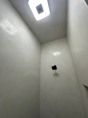Minimalist shower space with a black showerhead and ceiling light.