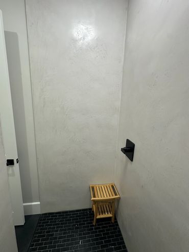 Minimalist bathroom corner with textured walls and small wooden stool.