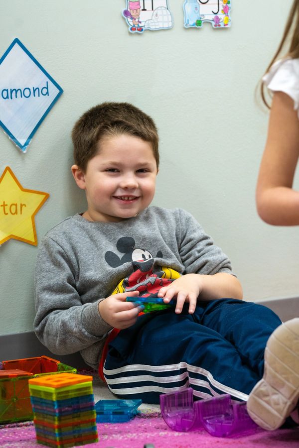 5 year old boy smiles and plays with magnatiles developing STEM skills