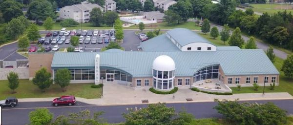 A modern, single-story building with a dome and large windows, surrounded by trees and parking lots.