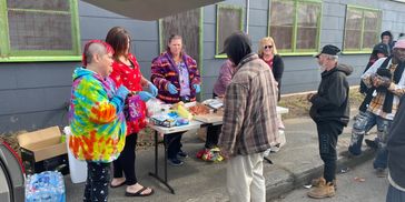 People gathered outdoors distributing and receiving food at a community table.