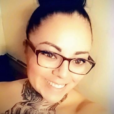Smiling woman with glasses and a neck tattoo.