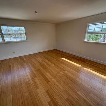 Empty room with wooden floor and two windows letting in natural light.