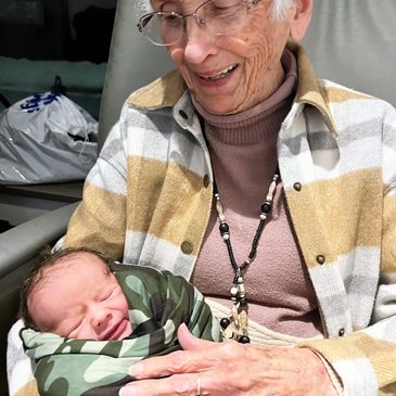 Elderly woman holding a newborn baby wrapped in a camouflage blanket.