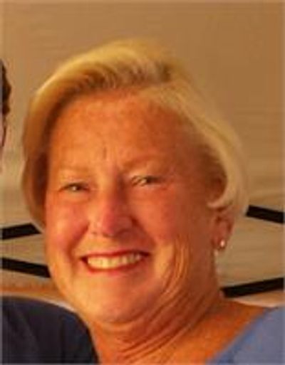 Smiling elderly woman with short blonde hair and pearl earrings.