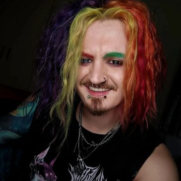 Person with colorful rainbow hair and facial piercings smiling.