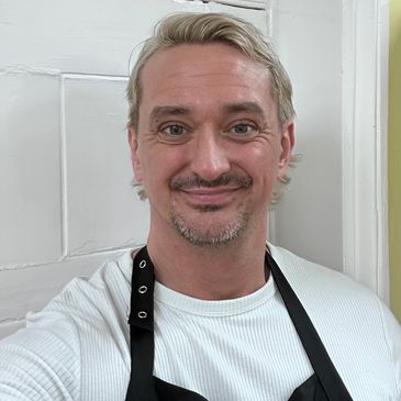 Smiling man wearing a white shirt and black apron.