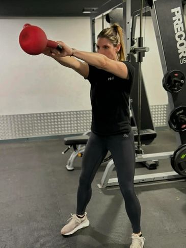 Woman performing kettlebell swings in a gym setting.