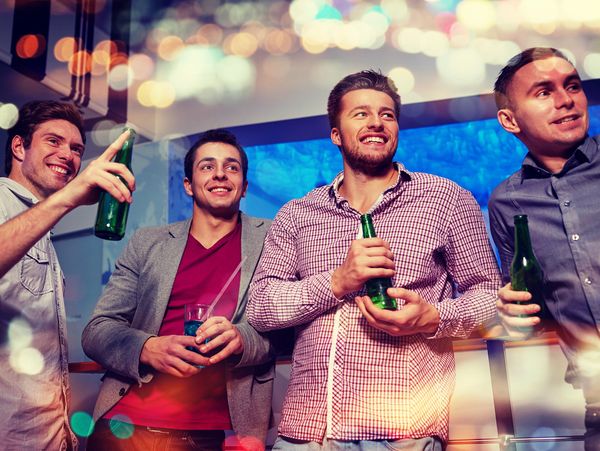 group of smiling male friends with beer bottles drinking and having fun in a nightclub