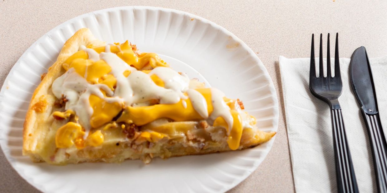 A slice of cheesy pizza with white sauce on a paper plate.