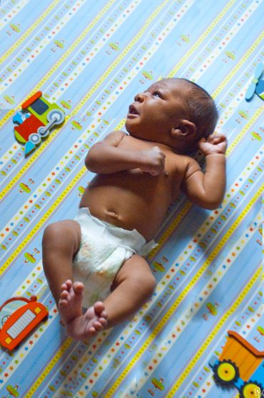 Newborn baby lying on a colorful patterned sheet with toy decorations.