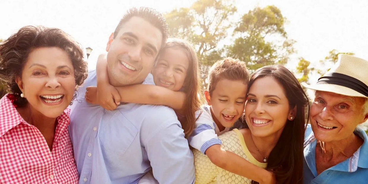 Happy multi-generational family smiling together outdoors in bright sunlight.