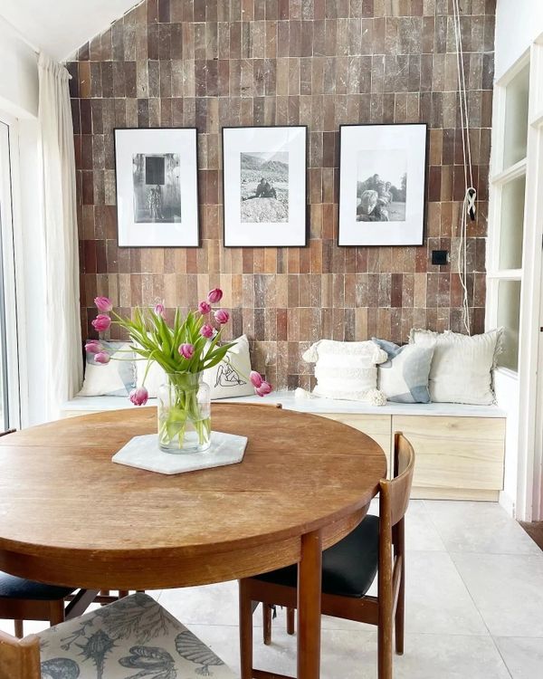 Cozy dining area with wooden table, tulip centerpiece, and framed photos on tiled wall.