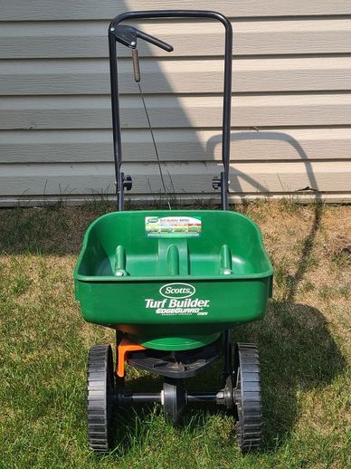 Scotts Turf Builder EdgeGuard spreader on grass in front of siding.