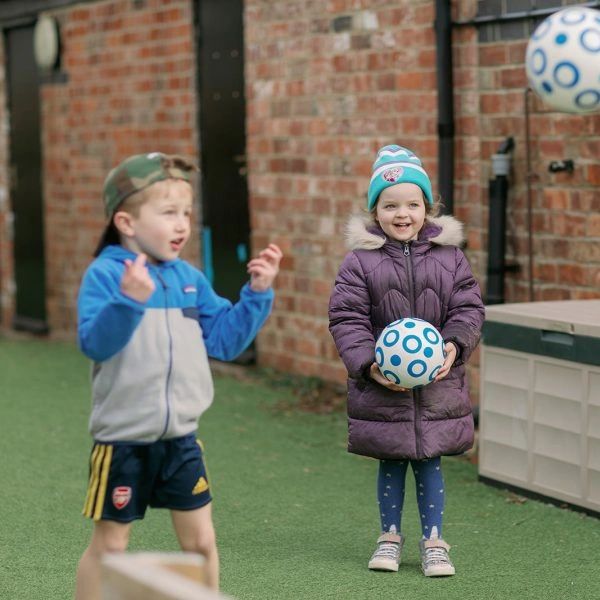 Two kids playing with blue and white balls outside.