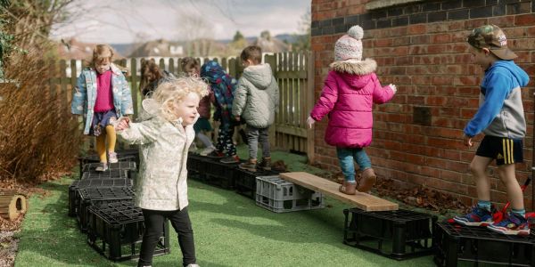 Children balancing on crates and wooden planks outdoors.