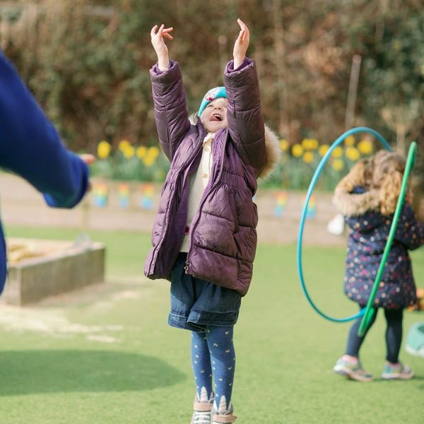 Child joyfully reaching up outside in winter clothing.