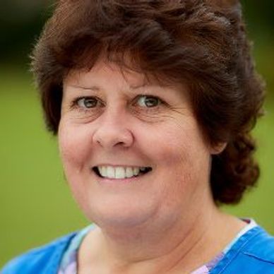 Smiling middle-aged woman with curly brown hair and blue top.