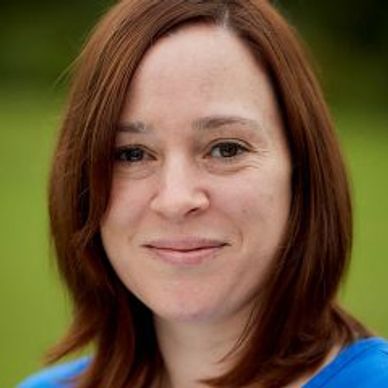 Smiling woman with brown hair and blue top outdoors.