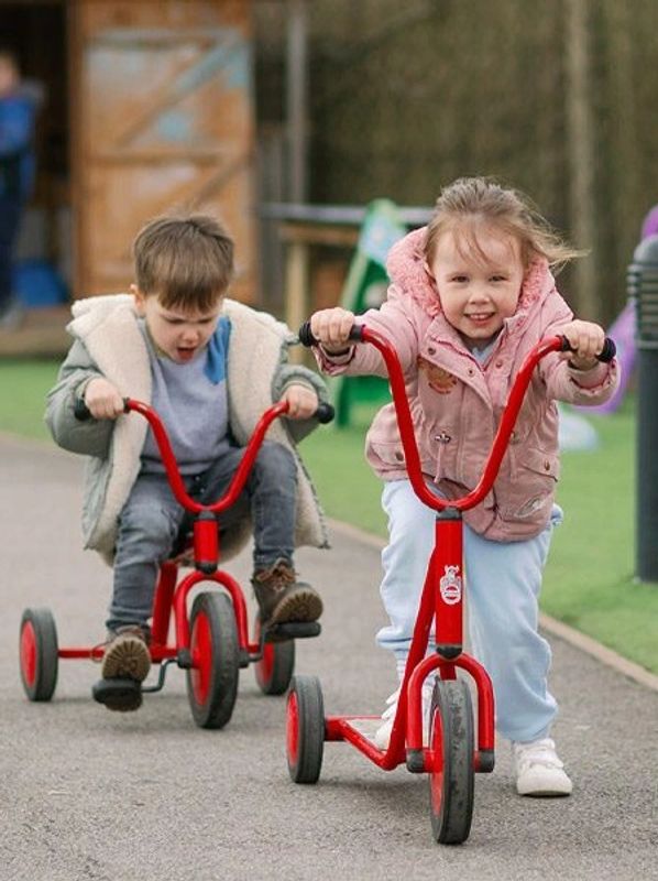 Two children riding red tricycles outdoors.