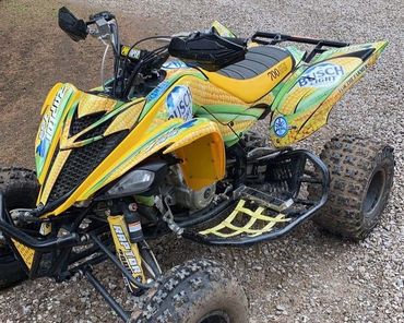 Yellow and green ATV with corn and Busch Light design on rocky ground.