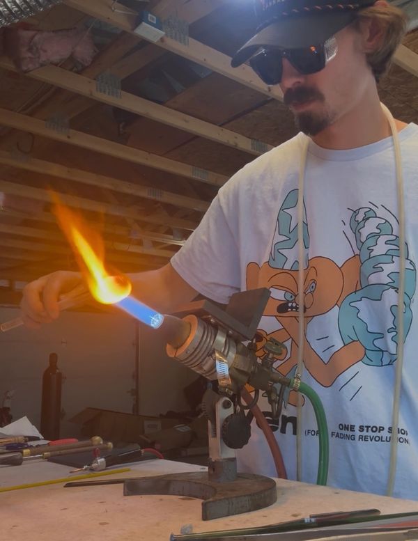 Man using a torch to heat glass in a workshop.