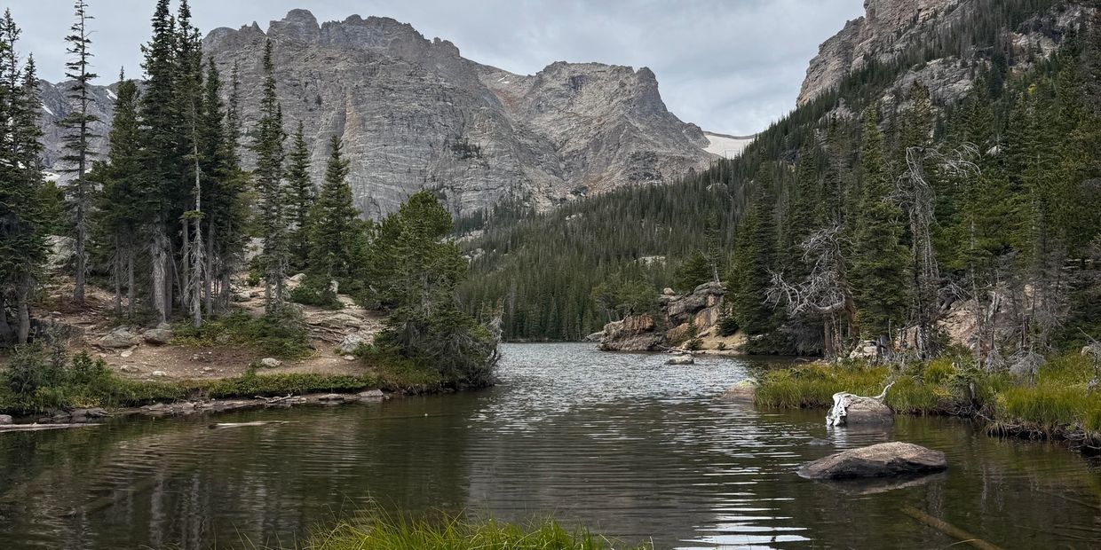 A serene mountain lake surrounded by evergreen trees under a cloudy sky.