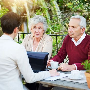 Elderly couple discussing with a professional outdoors at a table.
