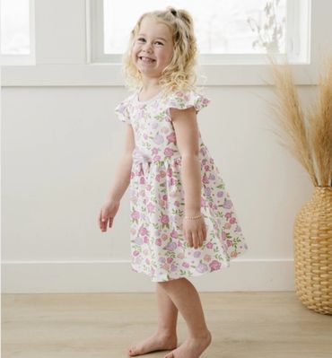 Smiling little girl in a floral dress standing barefoot indoors.