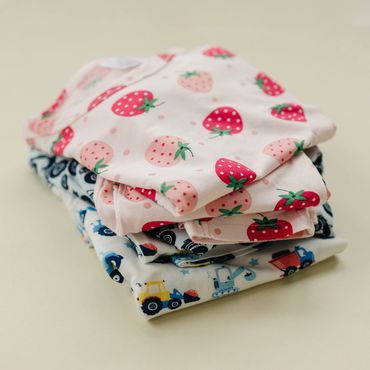 Folded baby clothes with strawberry and vehicle patterns.