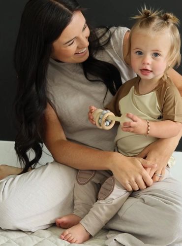 A mother joyfully holds her toddler, who is playing with a wooden rattle.