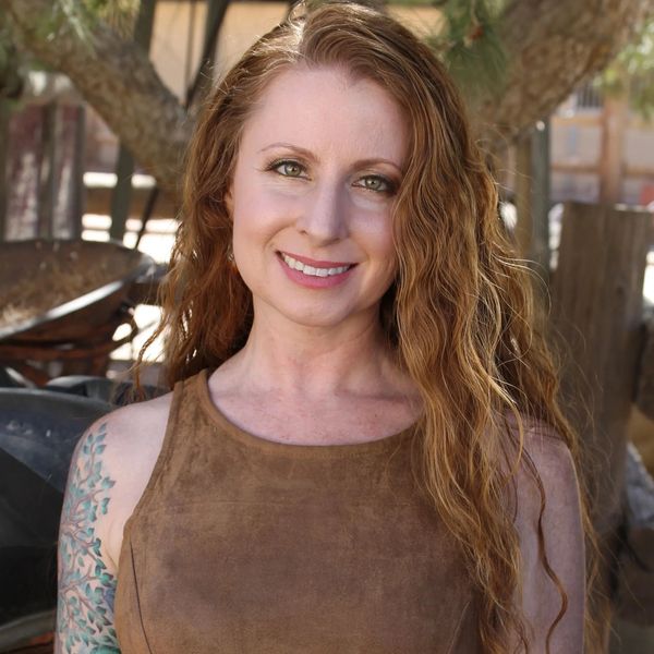 Smiling woman with long curly hair and tattooed arm outdoors.