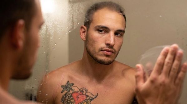 Man with chest tattoos looking into a foggy mirror.