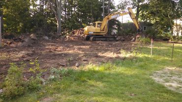 Yellow Deere excavator working on clearing a wooded area.