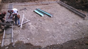 Workers pouring concrete into foundation forms at a construction site.