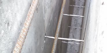 Close-up of concrete wall with embedded rusted steel rebar and metal ties.