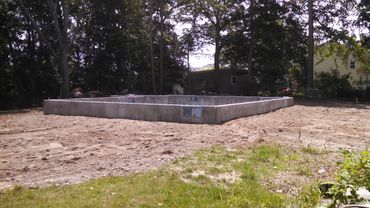 Concrete foundation for a new building in a cleared plot near trees.