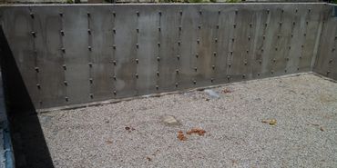 A concrete wall with bolts and a gravel-covered ground.